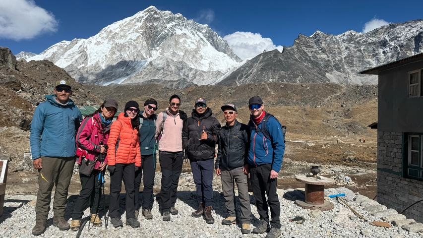 Group of mountaineers posing with snowy peaks in the background.