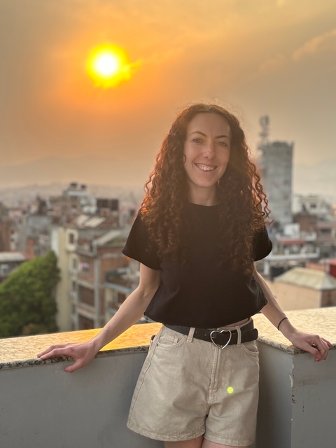 Person standing on a balcony overlooking a cityscape at sunset.
