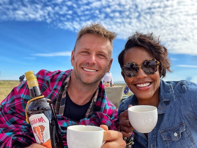       Smiling couple with drinks and a landscape in the background.
  