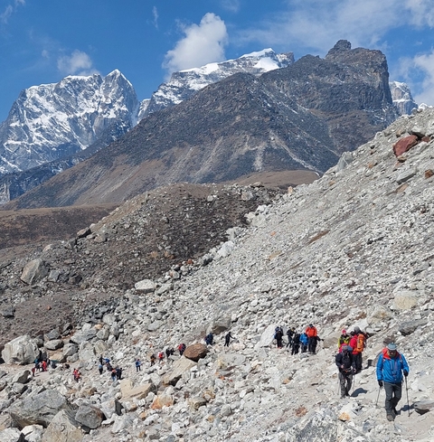 Hikers walking on rocky terrain with mountains in the background.