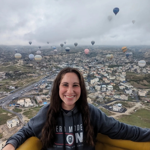       Woman in a hot air balloon with numerous balloons over a city.
  