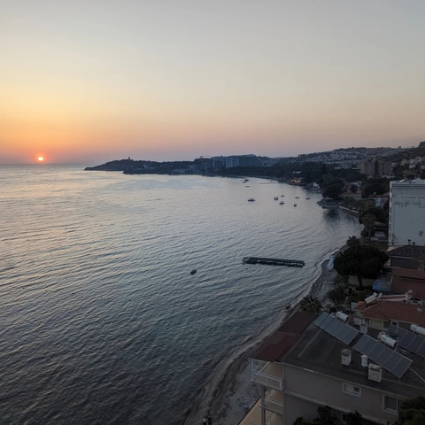 Coastal cityscape with the sun setting on the horizon.