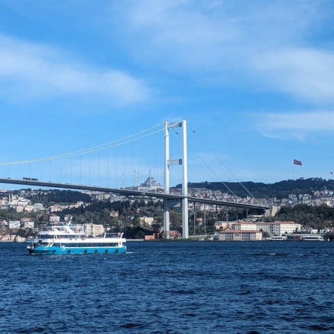 A bridge crossing over a body of water with a cityscape and mosque in the background, under a blue sky.
