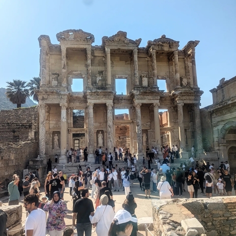       Crowd of people gathered at an ancient amphitheater with statues embedded in the structure.
  