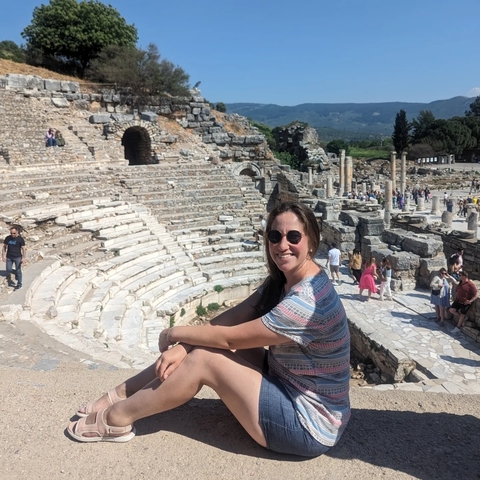       Person sitting on steps in an amphitheater area with various ancient stone ruins and columns.
  
