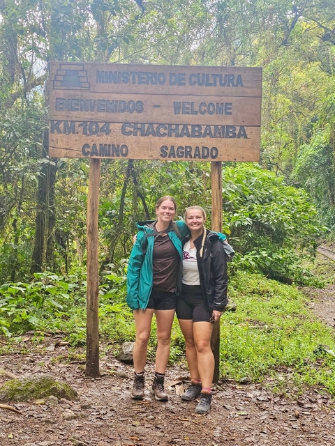 Two people smiling and standing before a sign and green foliage.