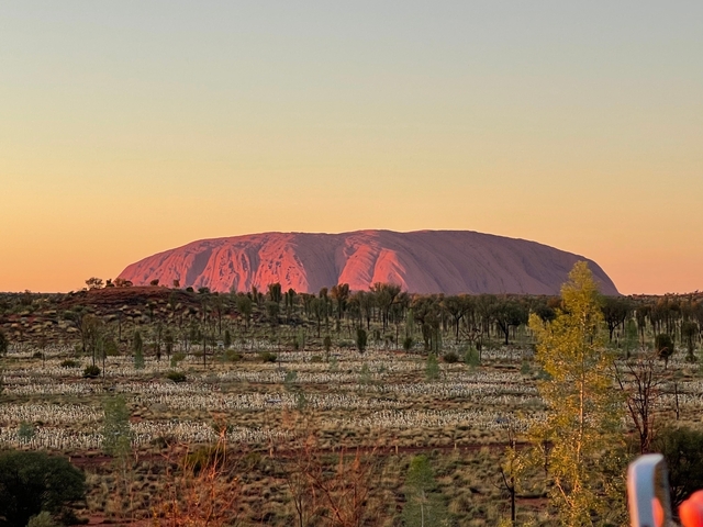       Sunset view of a famous rock formation surrounded by trees.
  