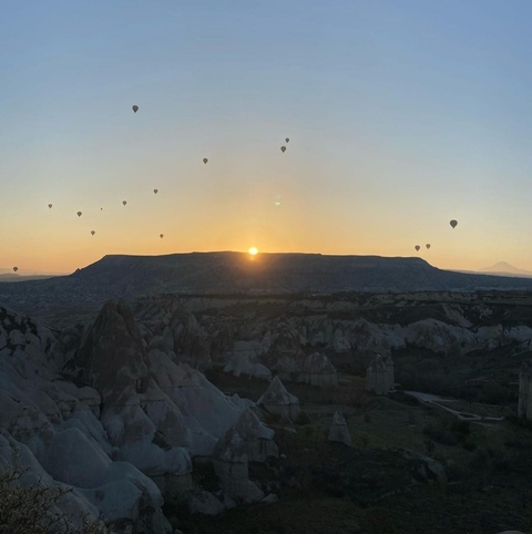       Hot air balloons floating at sunrise over rocky formations.
  