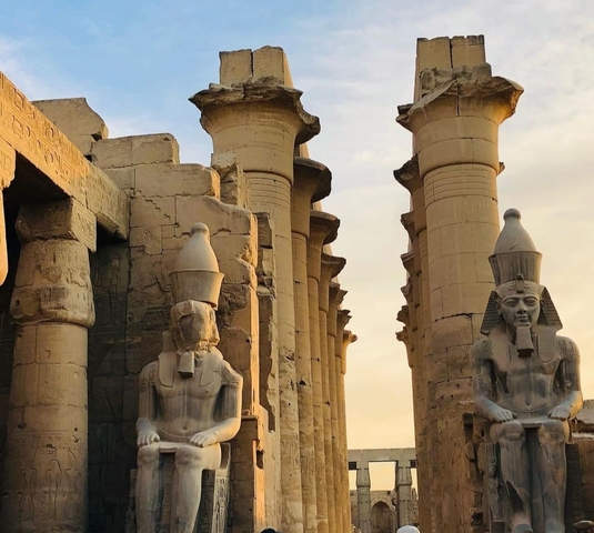 Row of statues and columns against a sunset sky.