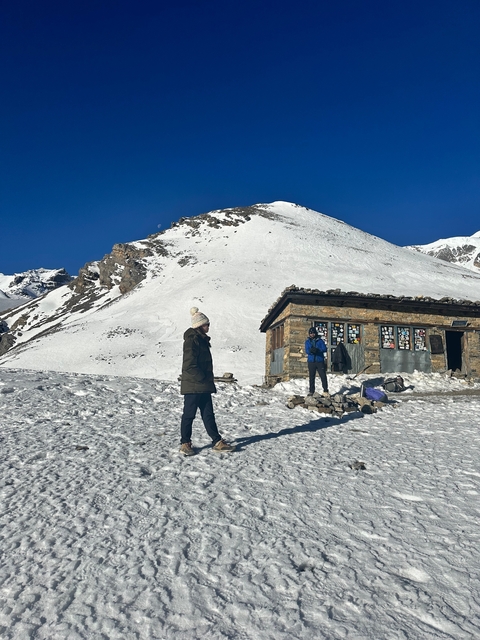       Person standing by a stone building in a snowy landscape.
  