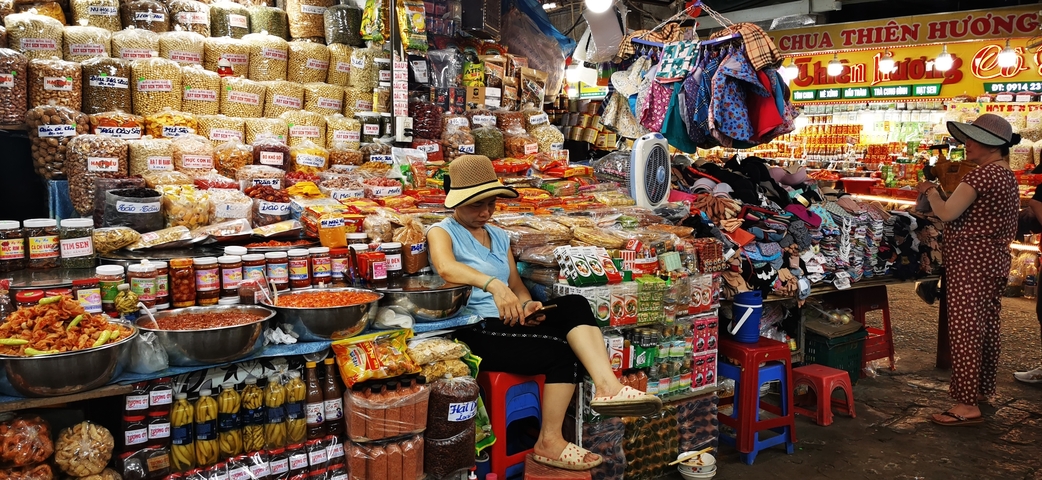       A bustling market stall with a woman resting.
  
