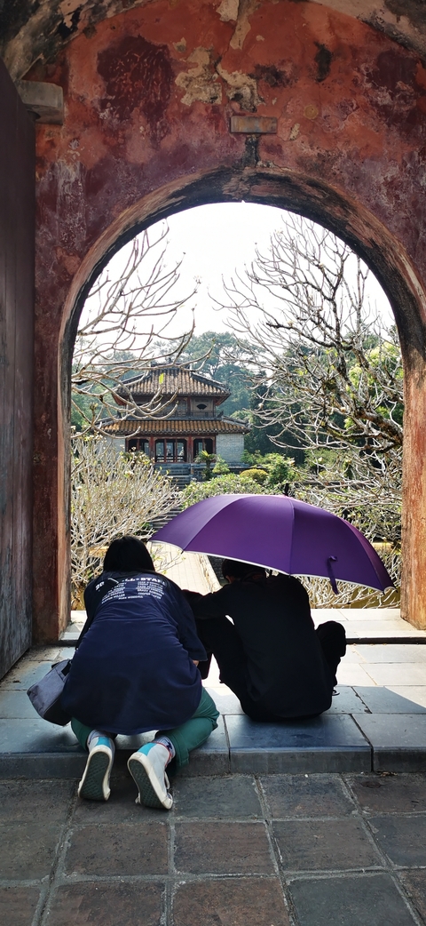       A traditional temple viewed through a gate with people and a purple umbrella.
  