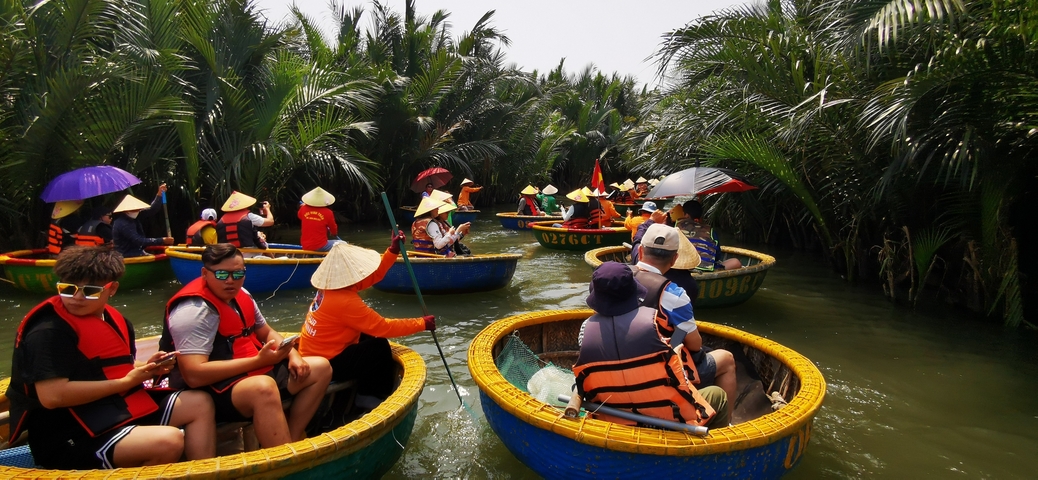       People rowing round boats in a lush canal.
  