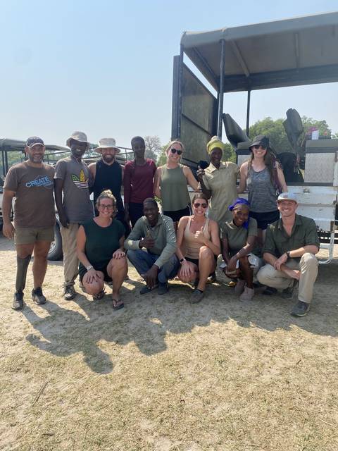 Group of tourists posing together in front of a safari truck.
