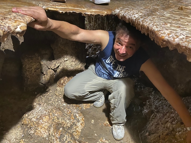 A person crouching inside a rocky cave.