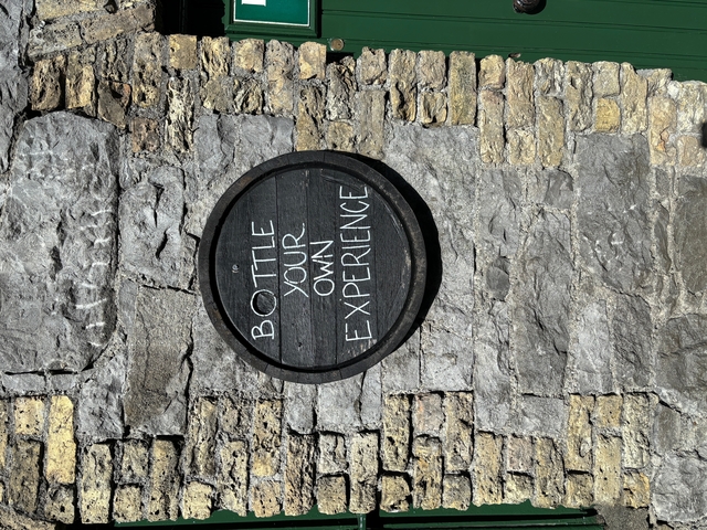 A wooden barrel with 'BOTTLE YOUR OWN EXPERIENCE' text on a stone wall.