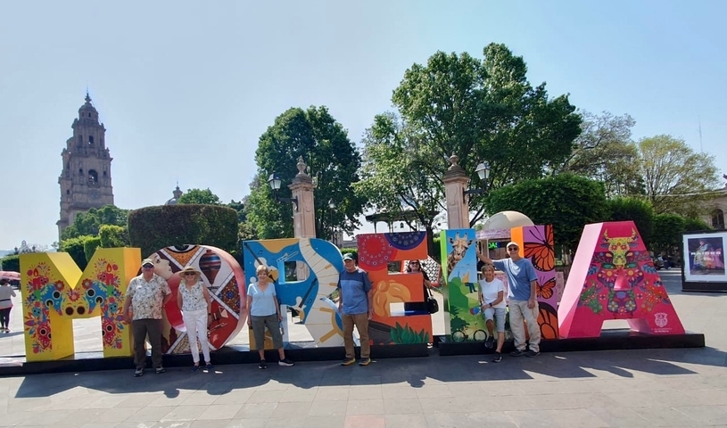       Group of people posing in front of colorful Morelia sign with tower in background.
  