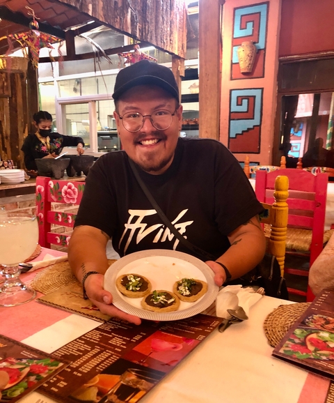       Person smiling holding a plate of food in a colorful restaurant.
  
