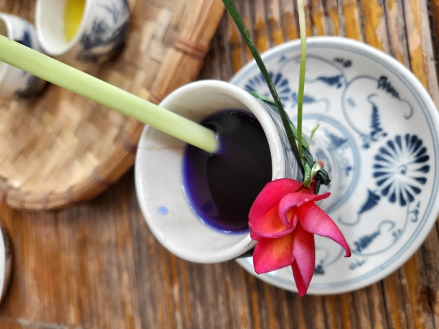 Cup with purple liquid and flower on a table.