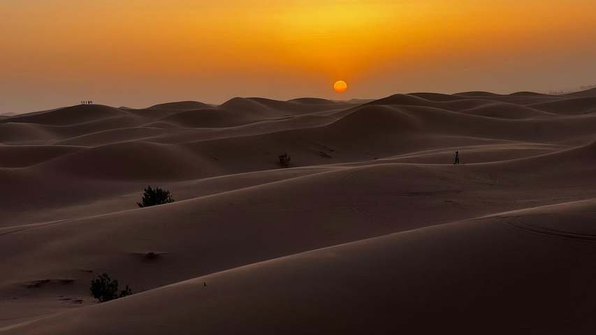 Sunset over sand dunes in a desert landscape.