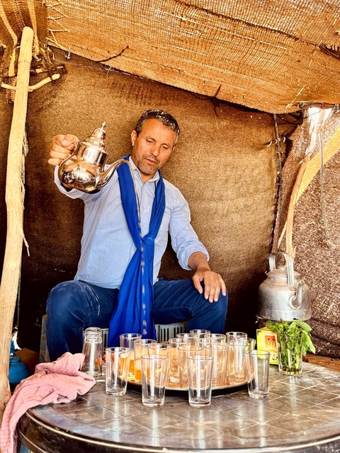 Man pouring tea, sitting inside a tent.