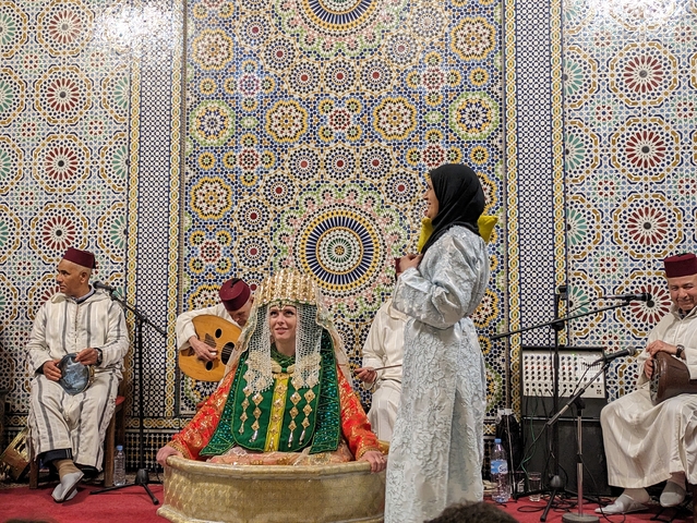       Group of people in traditional clothing with intricate mosaic backdrop.
  