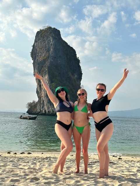 Three people posing in front of a large rock in the sea.