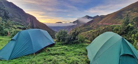 Tents set up in a valley with mountains at sunset.