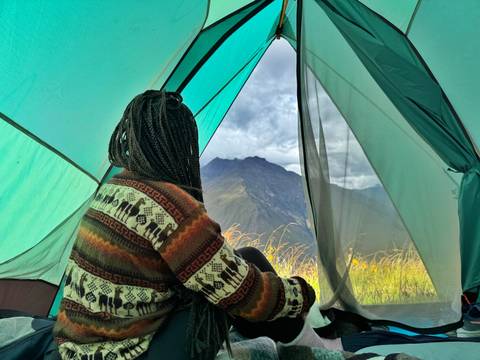 Woman looking out from a tent with mountain view.