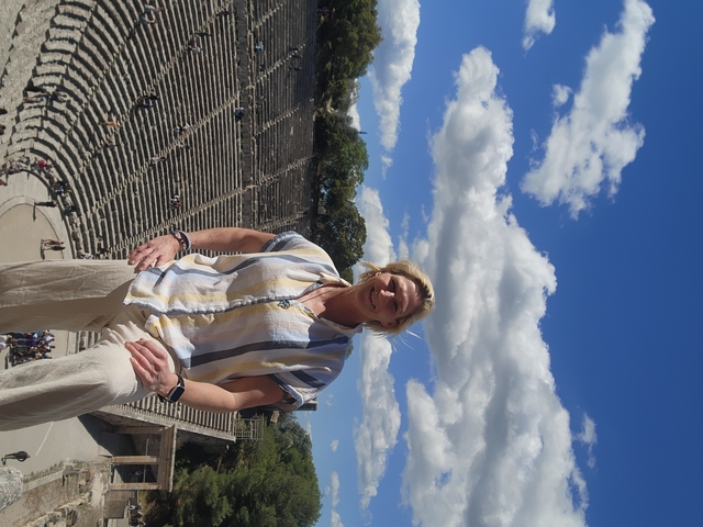       Person posing at an ancient amphitheater with a clear sky.
  