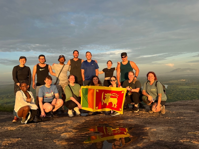 Group of people posing with a Sri Lankan flag at sunset.