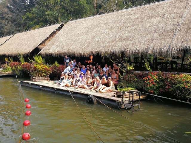       Group of people on a raft near a hut over water.
  