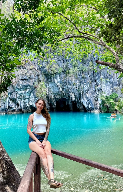 Woman posing in front of a cave with turquoise water.