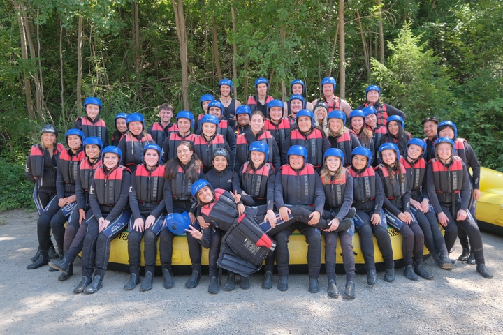 A large group of people posing in rafting gear in a forested area.