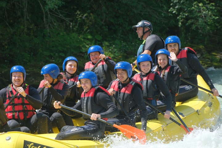 A group of people rafting on a river, smiling and waving.