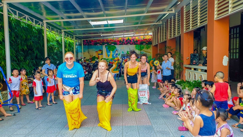 Group of women participating in a sack race at a community event surrounded by children.