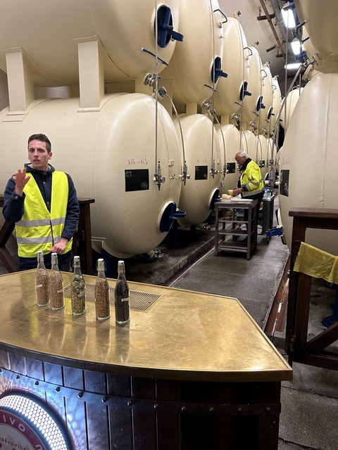 People working inside a cellar with large storage tanks.