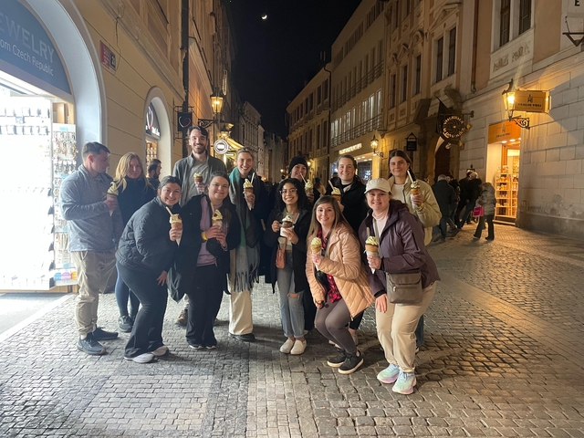 Large group of people enjoying ice creams in a lit street at night.