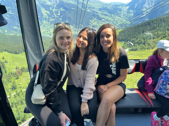 Three women in a cable car with a mountainous view.