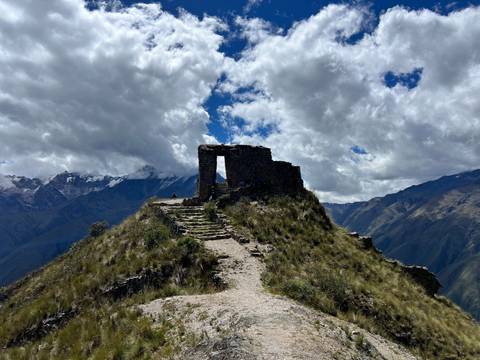Ruined structure on a mountainous path under a cloudy sky.