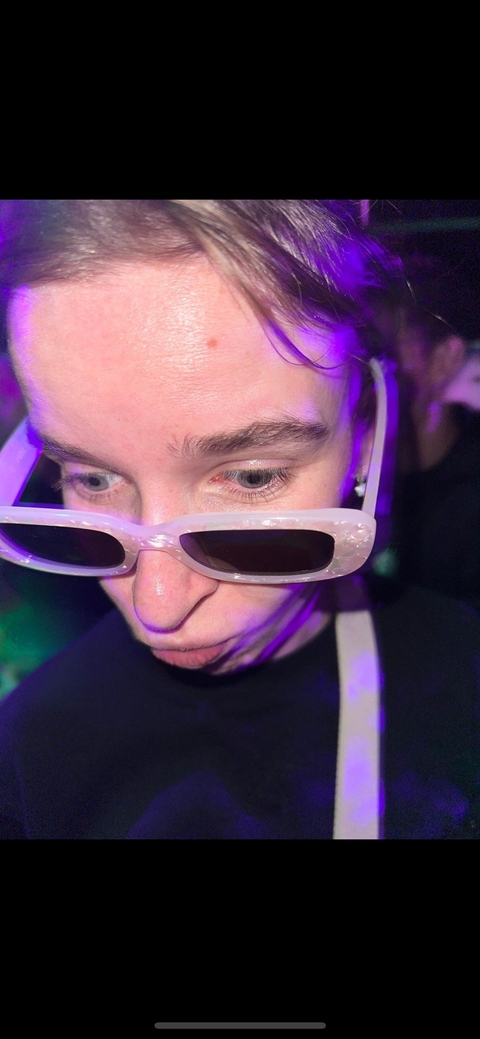 Close-up of a person's face with sunglasses under club lighting.