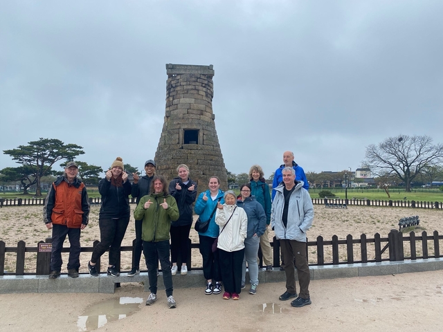 Group of people posing in front of an ancient stone tower.