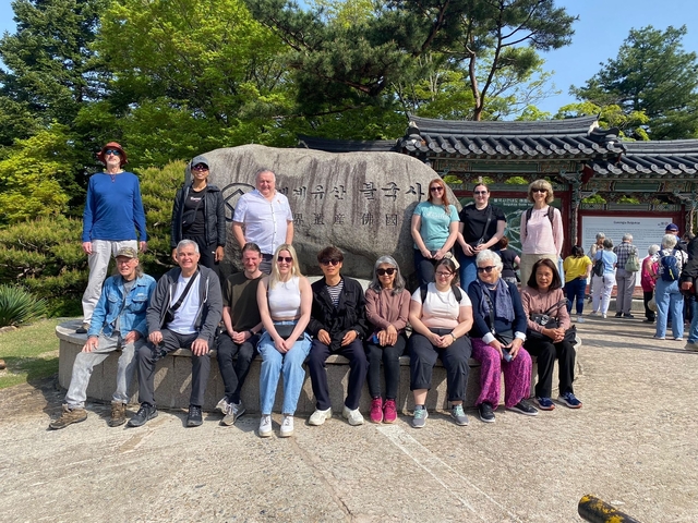 Group of people posing in front of a stone monument with traditional Korean signage.