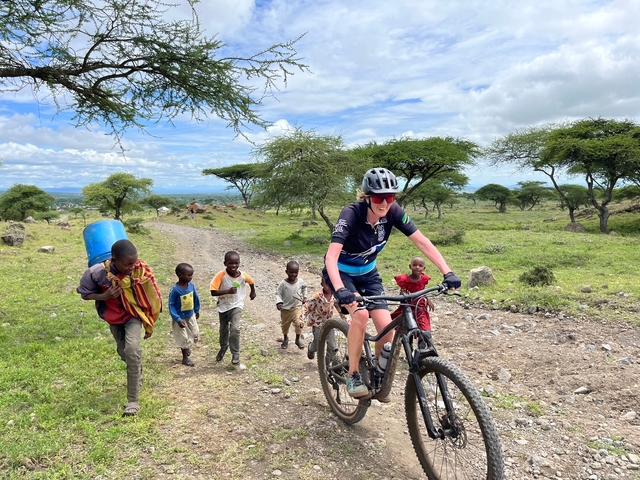 Cyclist and children on a dirt road with bicycles in rural landscape.