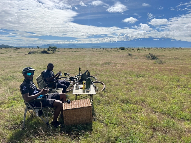 Cyclists taking a break in a grassy field with mountains in the distance.