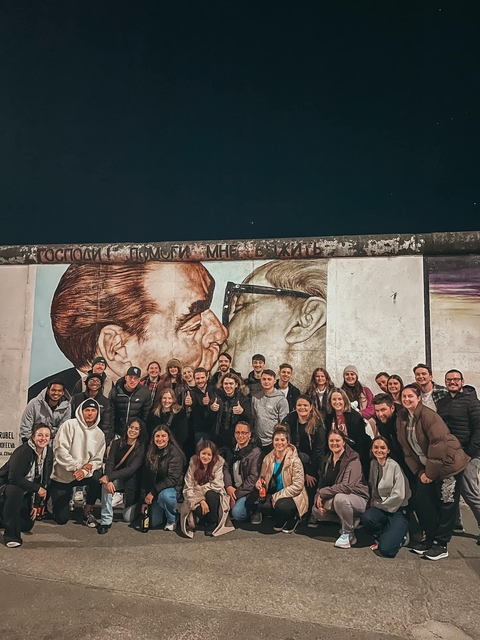 Large group in front of Berlin Wall mural.