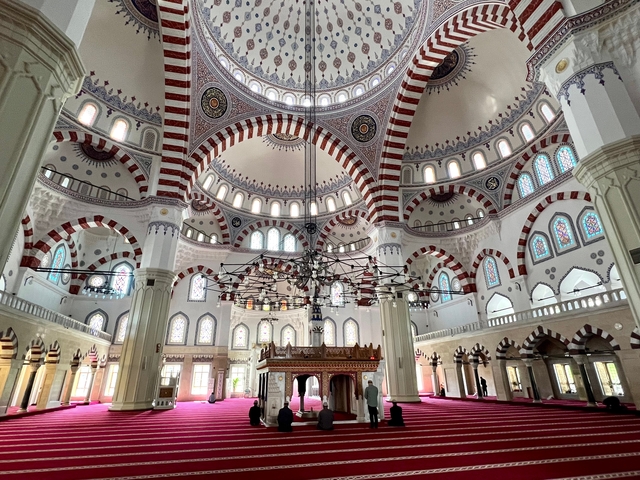       Interior of a richly decorated mosque with arches, columns, and chandeliers.
  
