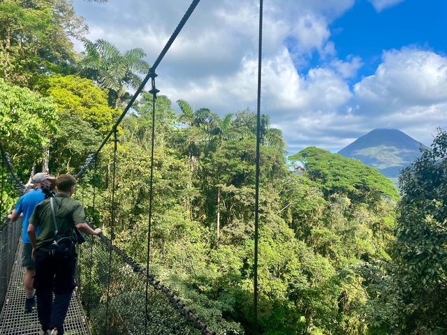 Tourists on a hanging bridge in a tropical setting with a volcano.