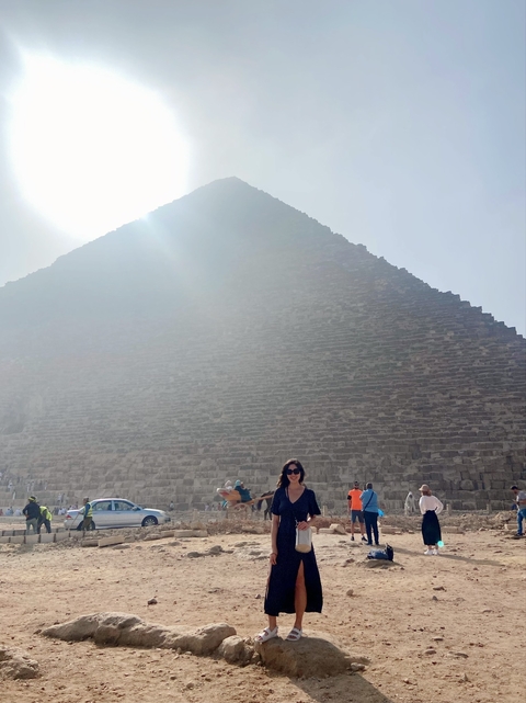 Person in front of a large pyramid with sunlight filtering through.