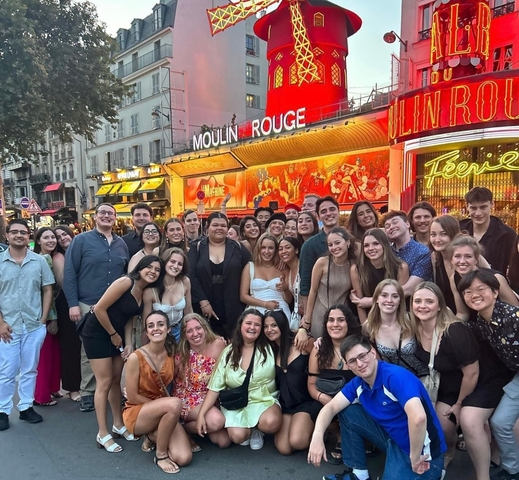 A night scene in front of Moulin Rouge with a large group of people posing.